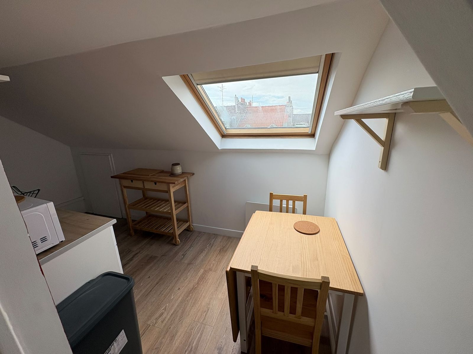 Coin repas sous la fenêtre de toit — table et chaises en bois, vue sur les toits de Lille