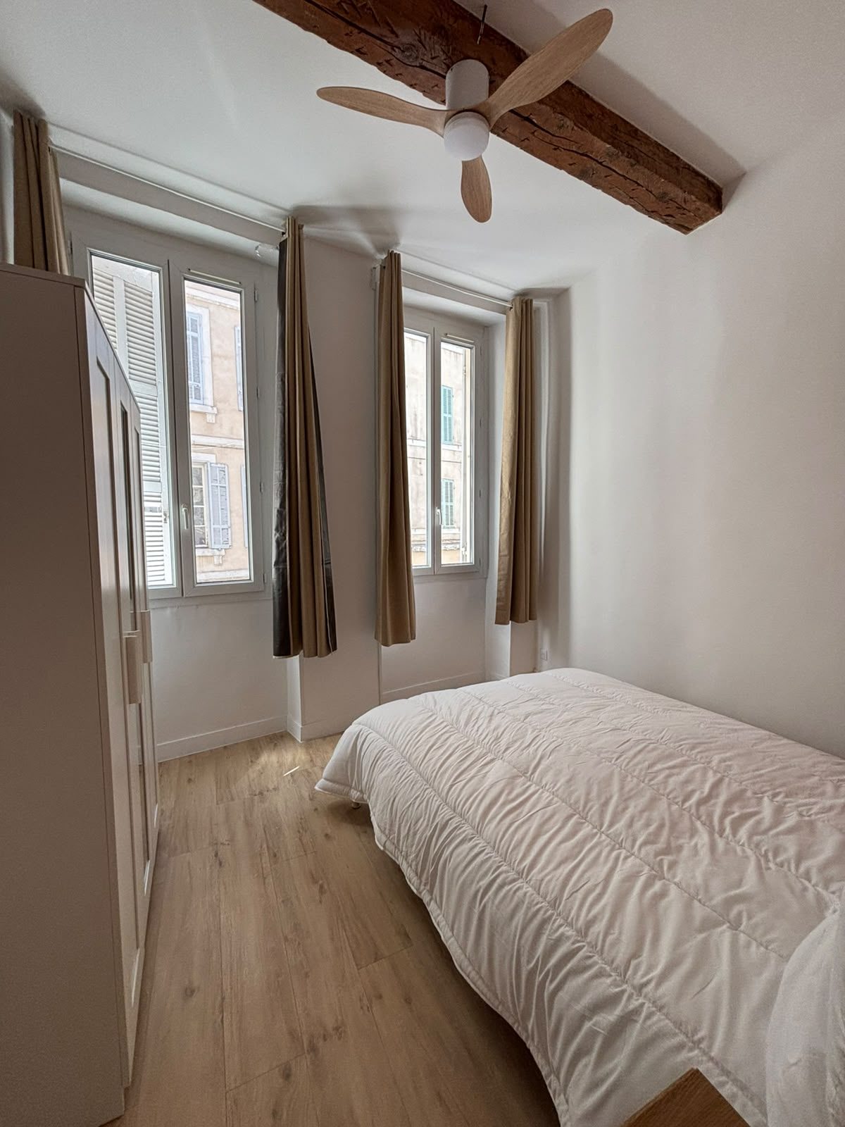 Chambre lumineuse du T2 meublé près du Vieux-Port — deux fenêtres, parquet clair et ventilateur de plafond