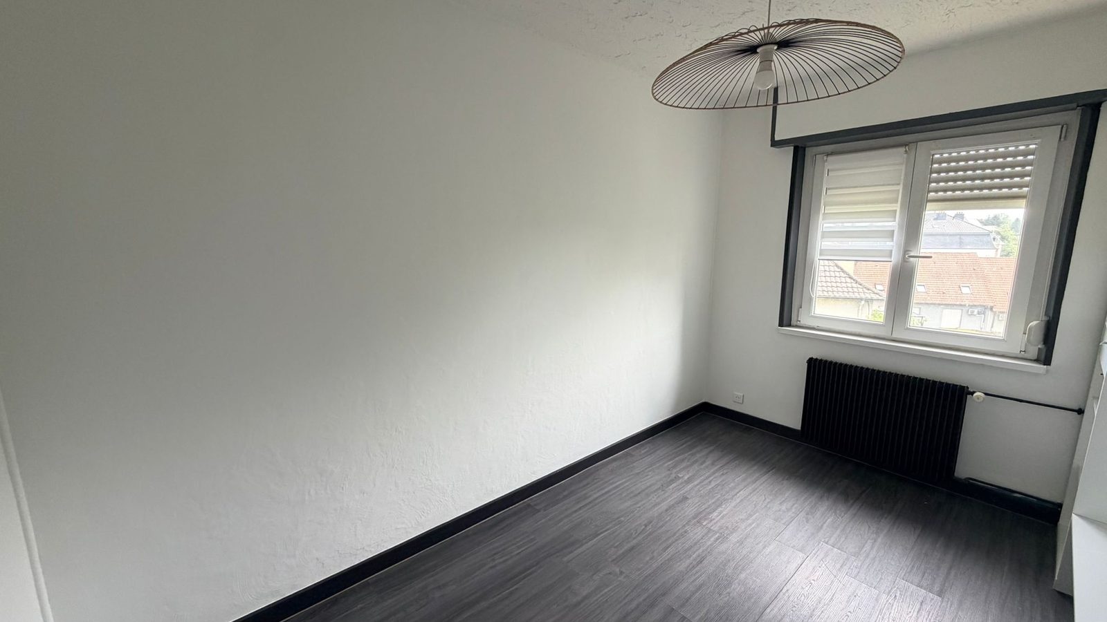 Chambre du 3 pièces à Mulhouse Dornach — murs clairs, parquet gris et grande fenêtre