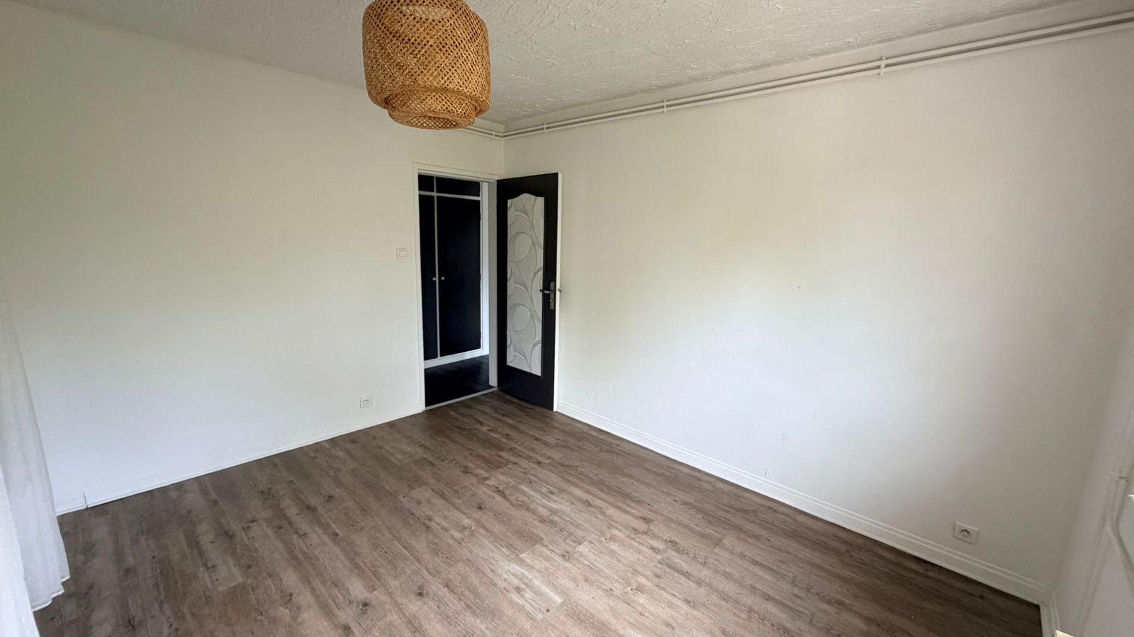 Deuxième chambre — parquet bois clair, suspension en rotin et porte rénovée