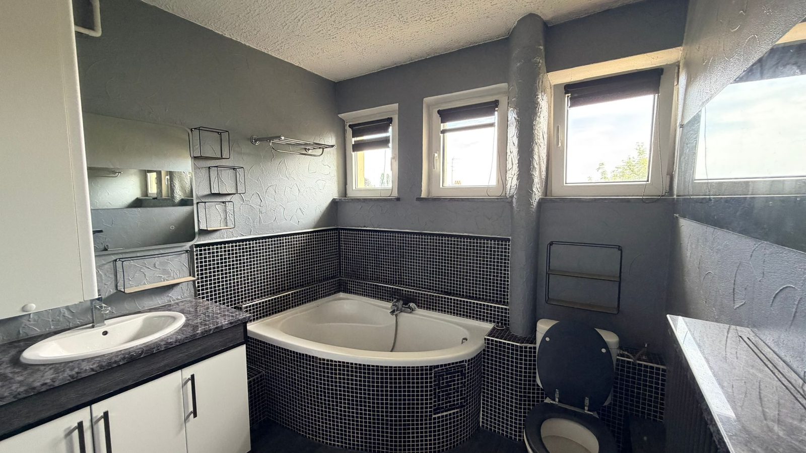 Salle de bains avec baignoire d’angle, faïence mosaïque, vasque et double fenêtre