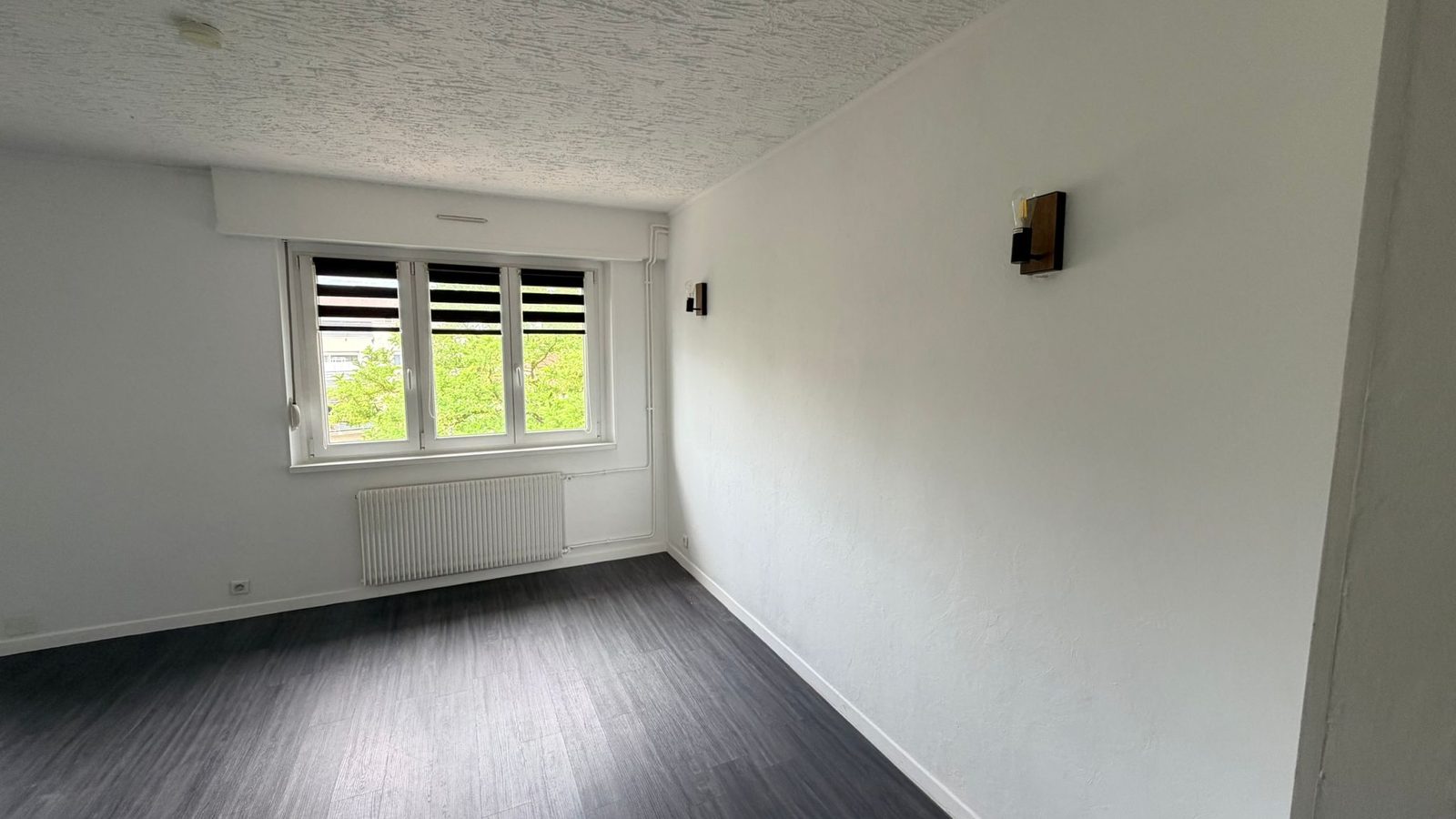 Pièce de vie du 3 pièces à Mulhouse Dornach — fenêtre triple vantail, appliques et parquet gris
